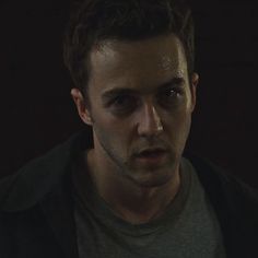 a young man stares into the camera while standing in front of a dark background with only one eye visible