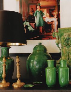 green vases are sitting on a table next to a lamp and pictures in the background