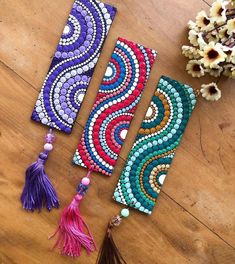 three colorful beaded bookmarks sitting on top of a wooden table next to flowers