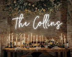 a table with candles and flowers on it in front of a brick wall that says the collinss