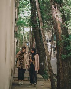 two women walking down a sidewalk between trees