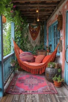 an orange hammock hanging from the side of a porch next to potted plants