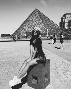 a woman sitting on top of a block in front of a building with a pyramid behind her