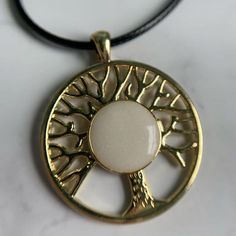 a gold tree of life pendant on a black cord with a white stone in the center