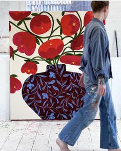 a woman walking past a painting with red flowers on it