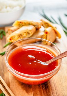 a bowl of ketchup sitting on top of a wooden cutting board with chopsticks