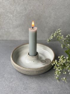 a single candle is lit on a plate with flowers in front of it and a gray background