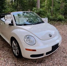 a white convertible car parked on gravel in front of trees