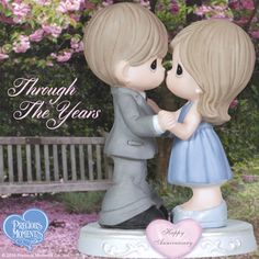 a figurine of two children kissing on a bench with pink flowers in the background