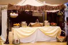 a table topped with lots of food under a white tent covered in lights and curtains