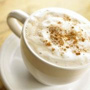 a white cup filled with whipped cream and cinnamon sprinkles on top of a saucer