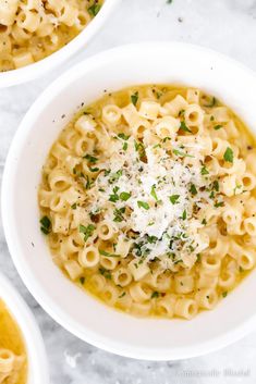 two white bowls filled with macaroni and cheese on top of a marble table