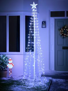 a lighted christmas tree in front of a house with a teddy bear sitting on the porch