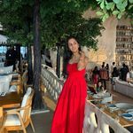 a woman in a red dress is standing near tables and chairs at an outdoor restaurant