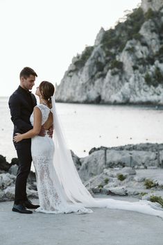 a bride and groom standing next to each other in front of the ocean