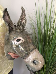 a person holding a fake donkey head in front of a potted plant with grass