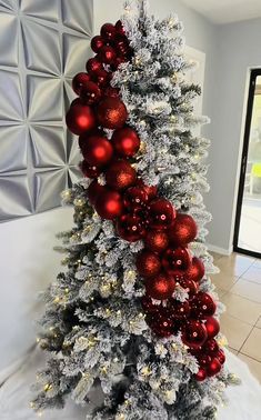 a decorated christmas tree with red and silver ornaments on it's top, in front of a wall