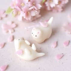 two small plastic animals sitting next to each other on a white surface with pink flowers in the background