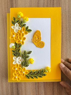 a handmade card with yellow flowers and a butterfly on the front, sitting on top of a wooden table