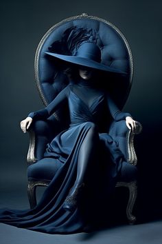 a woman in a blue dress and hat sitting on a chair with her legs crossed