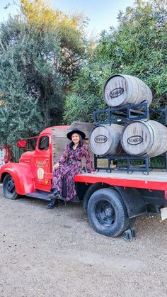 a woman sitting on the back of a red truck with barrels stacked on it's flatbed