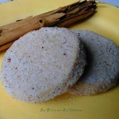 two cookies on a yellow plate next to an orange and white napkin with cinnamon sticks