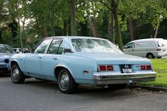 an old blue car is parked on the side of the road in front of other cars