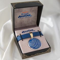 a blue and gold necklace in a black box on a white cloth covered tablecloth