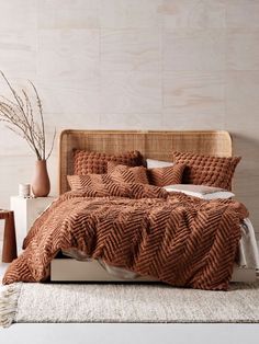 a bed with brown comforter and pillows in a white room next to a plant