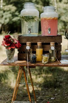 some drinks are sitting on a table with flowers in vases and jars next to each other