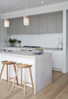 two wooden stools sit in front of an island counter with white walls and cabinets