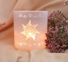 a lit candle sitting on top of a bed next to some purple flowers and a pink blanket