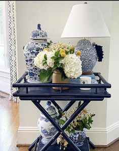 a table with vases and flowers on it in front of a lamp next to a window