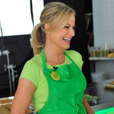 a woman in an apron smiles as she prepares food