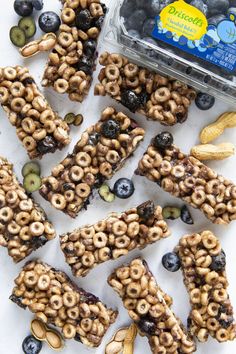 an assortment of cereal bars with blueberries, bananas and other foodstuffs on a white surface