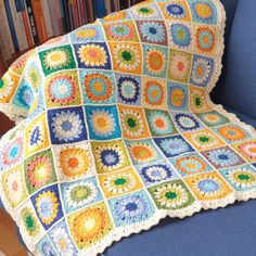 a crocheted granny's afghan sits on a blue chair in front of bookshelves