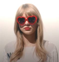 a woman with red heart shaped sunglasses on her face and long blonde hair in front of a white wall