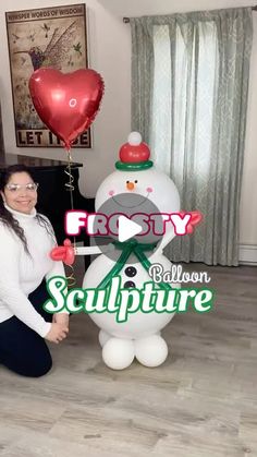 a woman kneeling down next to a large balloon snowman with a heart on it