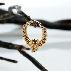 a gold ring with beads hanging from it's side on a branch in front of some branches