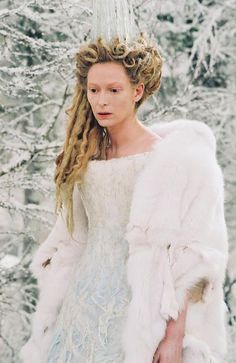 a woman with long blonde hair wearing a white dress and fur coat in the snow