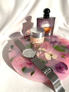 an assortment of perfumes and watches on a pink flowered tray with white fabric