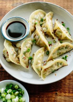 some dumplings are sitting on a plate with sauce and green onions next to it