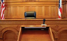 an empty courtroom with the judge's chair in front of it and american flags on the wall