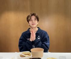 a young boy sitting at a table with food on it and his hands folded in front of him