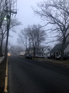 an empty street with houses and trees in the background on a foggy winter day