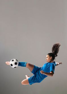 a young woman kicking a soccer ball in the air with her legs spread out,