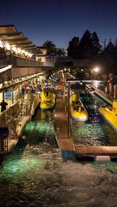 several yellow boats are docked in the water near a dock at night with people standing on it