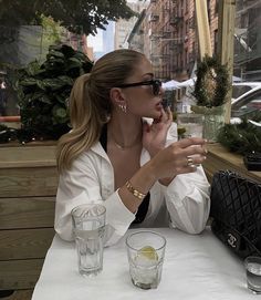 a woman sitting at a table in front of a window holding a cell phone to her ear