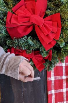 a person is holding a piece of paper in front of a christmas wreath with red bows