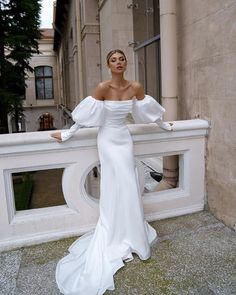 a woman standing on top of a balcony next to a white wall wearing a dress